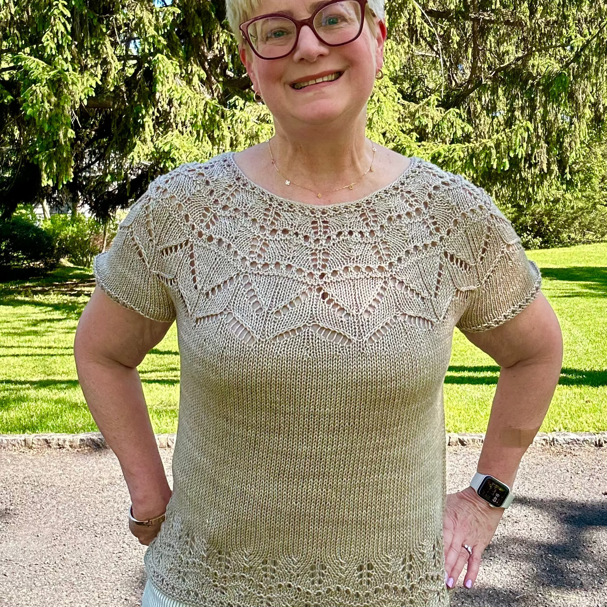 Woman wearing a beige lace top standing outdoors with trees in the background