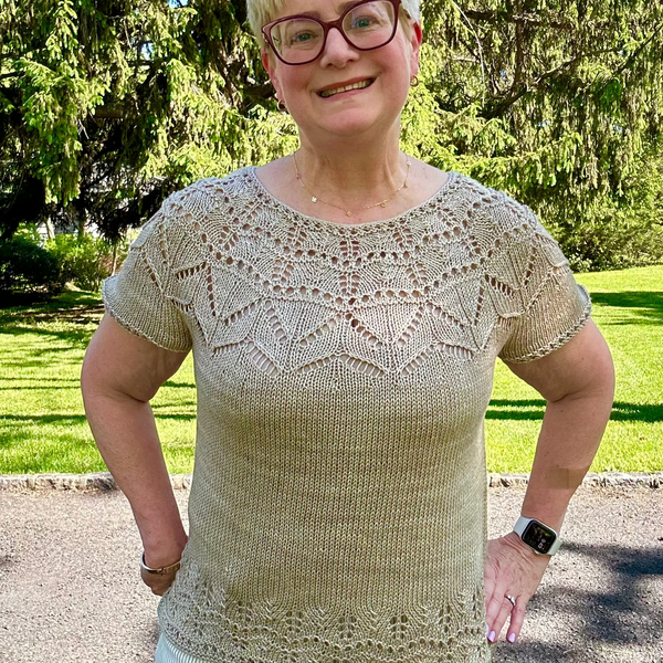 Woman wearing a beige lace top standing outdoors with trees in the background