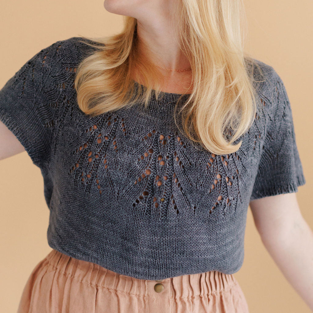 Woman wearing a dark blue knitted top with intricate patterns on a beige background